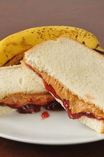 the sandwich is cut in half and sitting next to a banana on a plate with ketchup