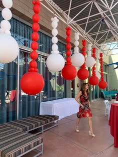 a woman standing under red and white balloons hanging from the ceiling in front of a building