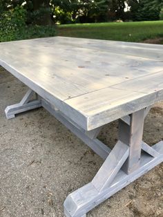 a wooden table sitting on top of a cement ground next to some grass and trees