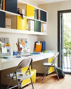 a desk with two chairs and yellow bookshelves on the wall in front of a sliding glass door