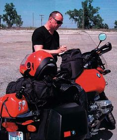 a man sitting on top of a red motorcycle next to a black bag and helmet