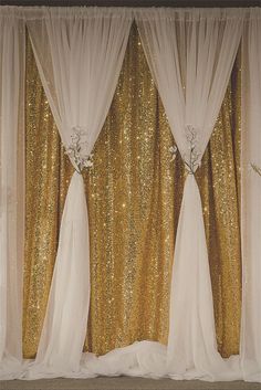 gold sequin backdrop with white drapes and flowers on the top, along with sheer curtains