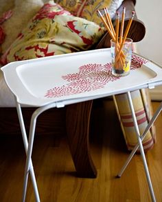 a white tray with some pencils on it next to a chair and pillows in the background