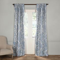 a white chair sitting in front of a window with blue paisley print curtains on it