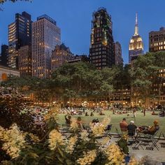 people are sitting and walking around in the park at night with skyscrapers in the background