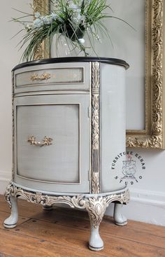 an old dresser with flowers on top in front of a mirror and gold trimming