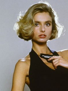 a woman in a black dress is holding a cell phone and looking at the camera