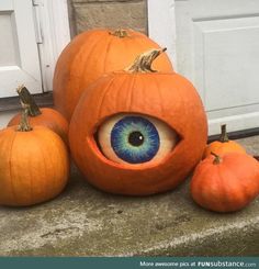 three pumpkins with an eye on them sitting in front of a door and two smaller pumpkins next to it