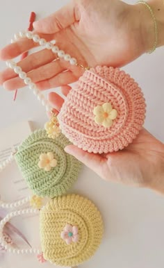 the hand is holding three small purses with flower decorations on them and pearls around it