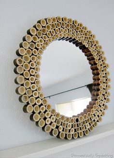 a circular mirror made out of wooden logs on top of a white shelf next to a window