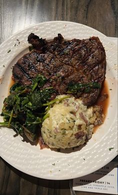 a white plate topped with steak, mashed potatoes and spinach on top of a wooden table