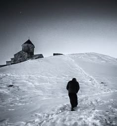 a man walking up a snow covered hill towards a church on top of a mountain