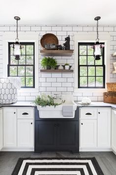 a kitchen with white cabinets and black counters, an area rug and potted plants