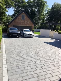 two cars parked in front of a brick driveway with a house behind them on the other side