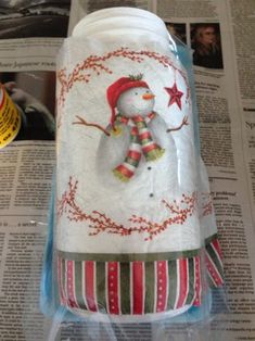 a glass jar with a snowman on it sitting on top of a news paper