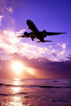 an airplane flying over the ocean at sunset with people watching from the beach below it