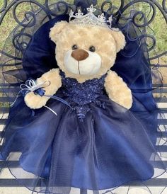 a teddy bear dressed in a blue dress sitting on a bench with a tiara