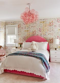 a bedroom with a pink bed and white furniture in front of a floral wallpapered wall