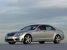 a silver mercedes cls parked in front of a gray sky with clouds behind it