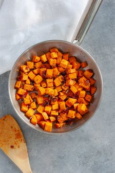 a pan filled with cooked sweet potatoes on top of a counter next to a wooden spoon