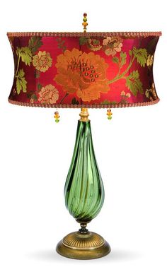 a green glass table lamp with a red shade on it's base and floral print lampshade