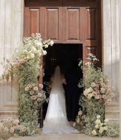 a bride and groom standing in front of an open doorway with flowers on either side