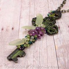 an old key with flowers and leaves attached to it on a wooden table next to a chain