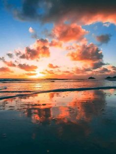 the sun is setting over the ocean with clouds in the sky and reflecting on the wet sand