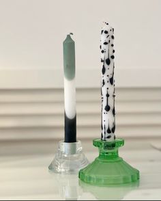 two black and white candles sitting on top of a green glass vase next to each other