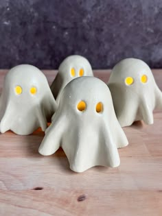 three white ghost figurines with yellow eyes on a wooden table next to each other