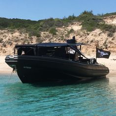 a black boat floating on top of the ocean next to a sandy beach and hill