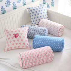 six decorative pillows on a bed with blue and pink flowers in the background, one has a monogrammed initial