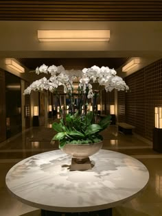 white flowers are in a vase on a marble table at the entrance to an office building