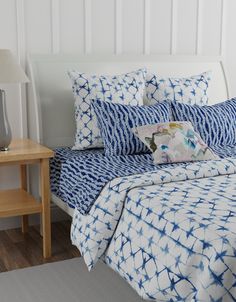 a bed with blue and white comforters on top of it next to a night stand