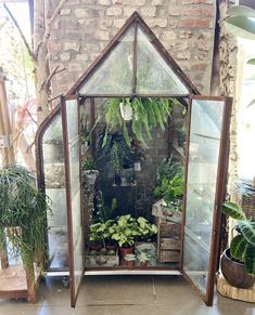 a house shaped greenhouse with plants in the front and on the side, surrounded by brick walls