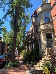 a tree in the middle of a sidewalk next to some buildings and cars parked on the street