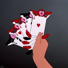 a hand holding four playing cards in front of a black background with red and pink hearts