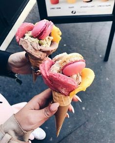 two people holding ice cream cones filled with different types of desserts and toppings