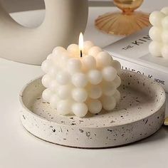 a white candle sitting on top of a table next to a book and glass vase