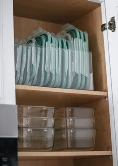 dishes are stacked on top of each other in a cupboard with clear plastic cups and containers