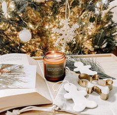 an open book on a table next to some cookies and a candle with snowflakes around it