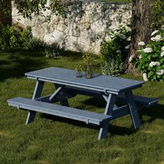 a blue picnic table sitting in the grass next to a stone wall and tree with white flowers