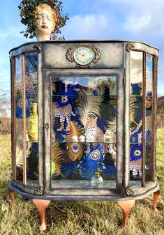 an artistic display cabinet in the middle of a grassy field with a clock on top