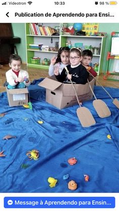 children are sitting in a cardboard boat on the floor with paper cut out to look like fish