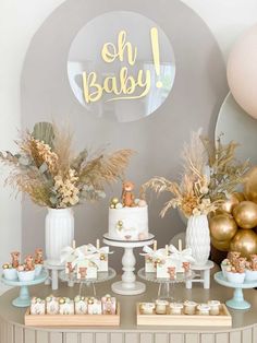 a table topped with cakes and desserts covered in frosting next to gold balloons