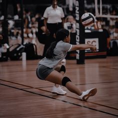 a woman is playing volleyball on the court while people watch from the stands behind her