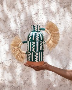 a hand holding a green and white vase with straws on it's sides