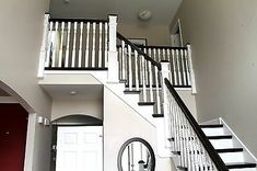 a white staircase with black handrails and a round mirror on the wall next to it