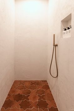 a bathroom with a shower head and brown floor tiles on the floor, along with a white wall