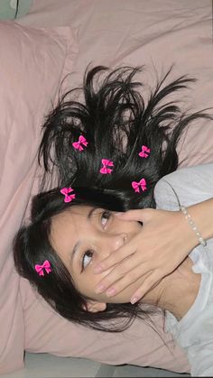 a woman laying in bed with her hands on her face and pink bows pinned to her hair